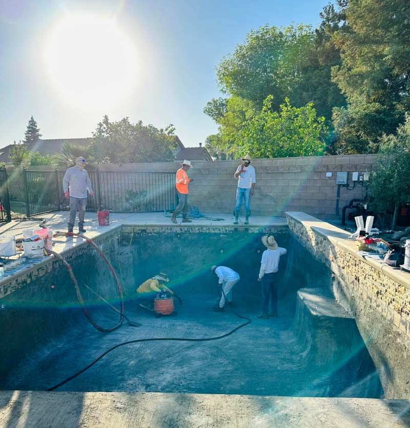 Professional pool plastering crew performing a full chip-out on a residential swimming pool in Bakersfield to prepare the surface for new premium quartz finish.