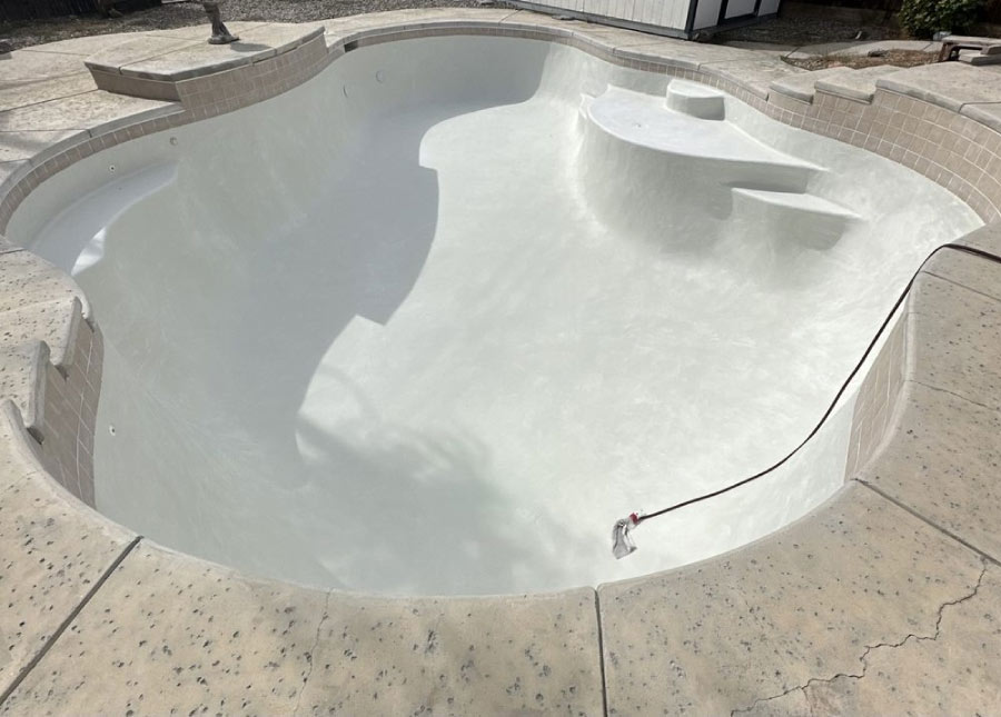Professional pool plastering crew in Bakersfield performing a full chip-out on a residential swimming pool to ensure a durable bond for new high-performance quartz finishing.